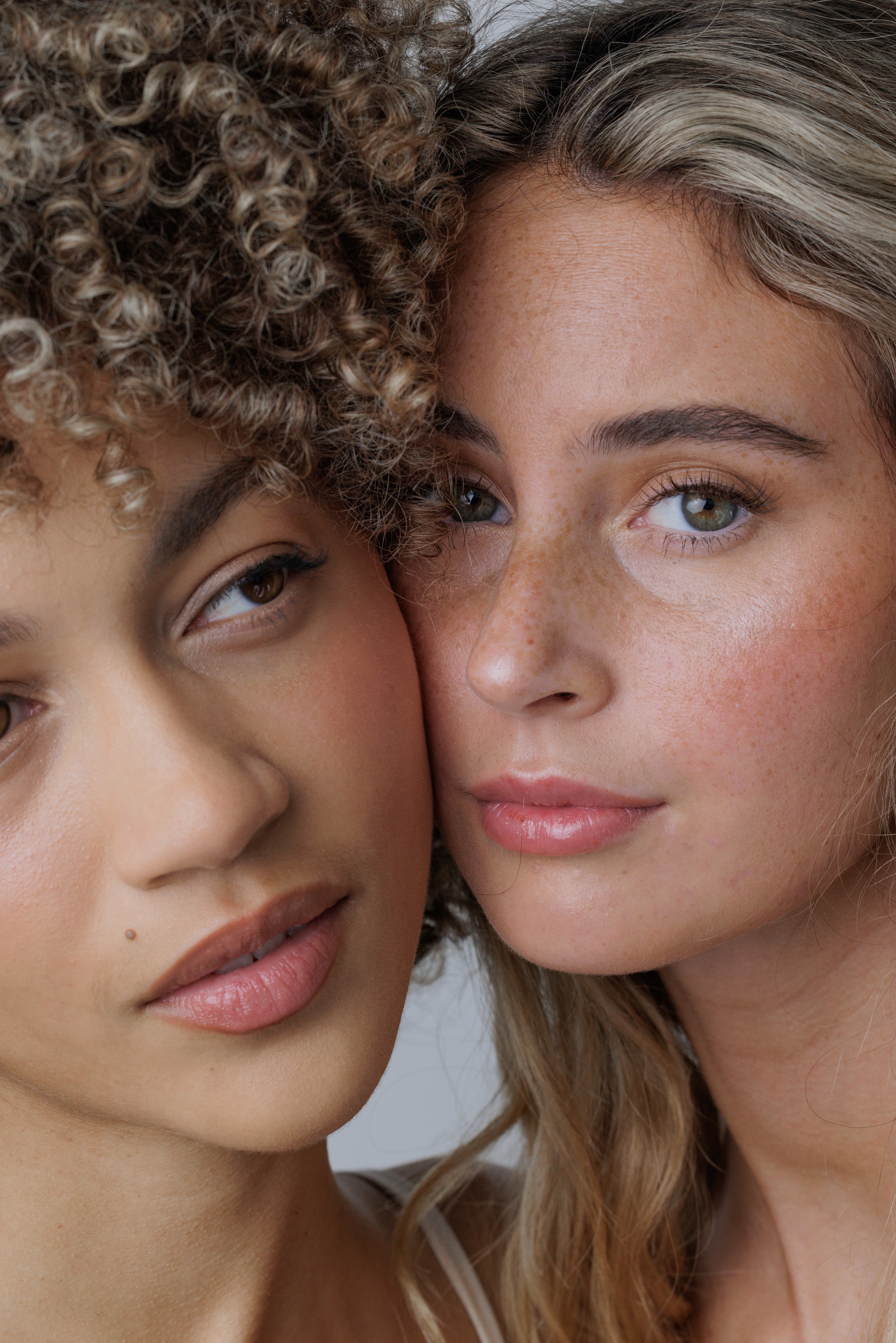 Two women with close-up faces, one with curly hair and the other with straight hair.