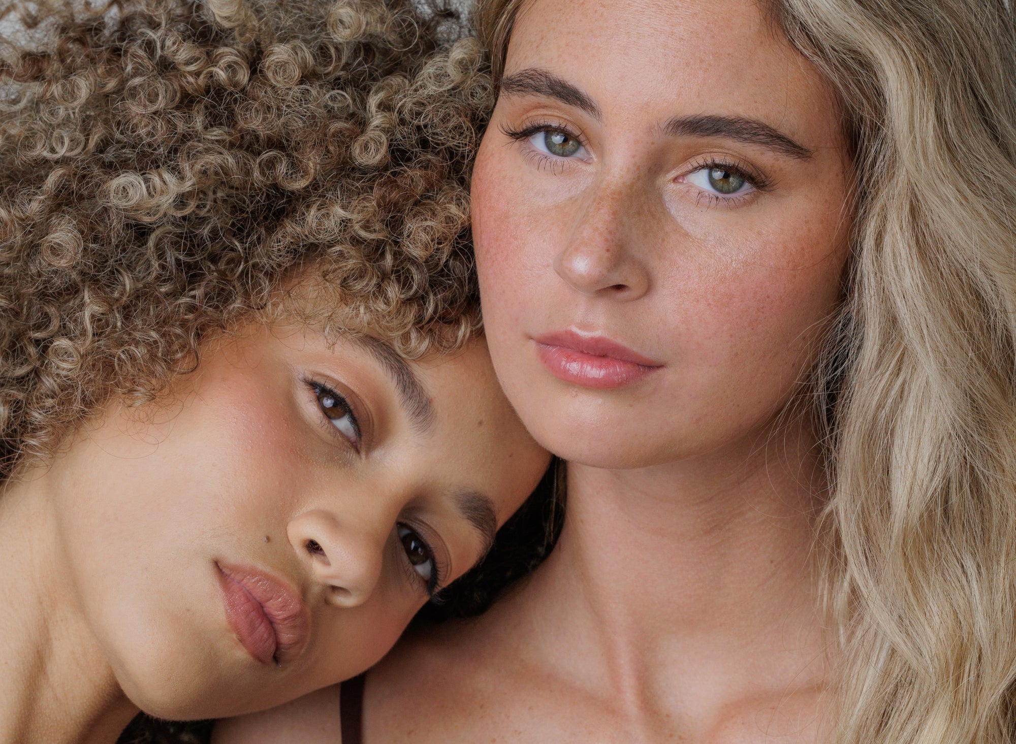 Two women with close-up of their faces, one with curly hair and the other with straight hair.