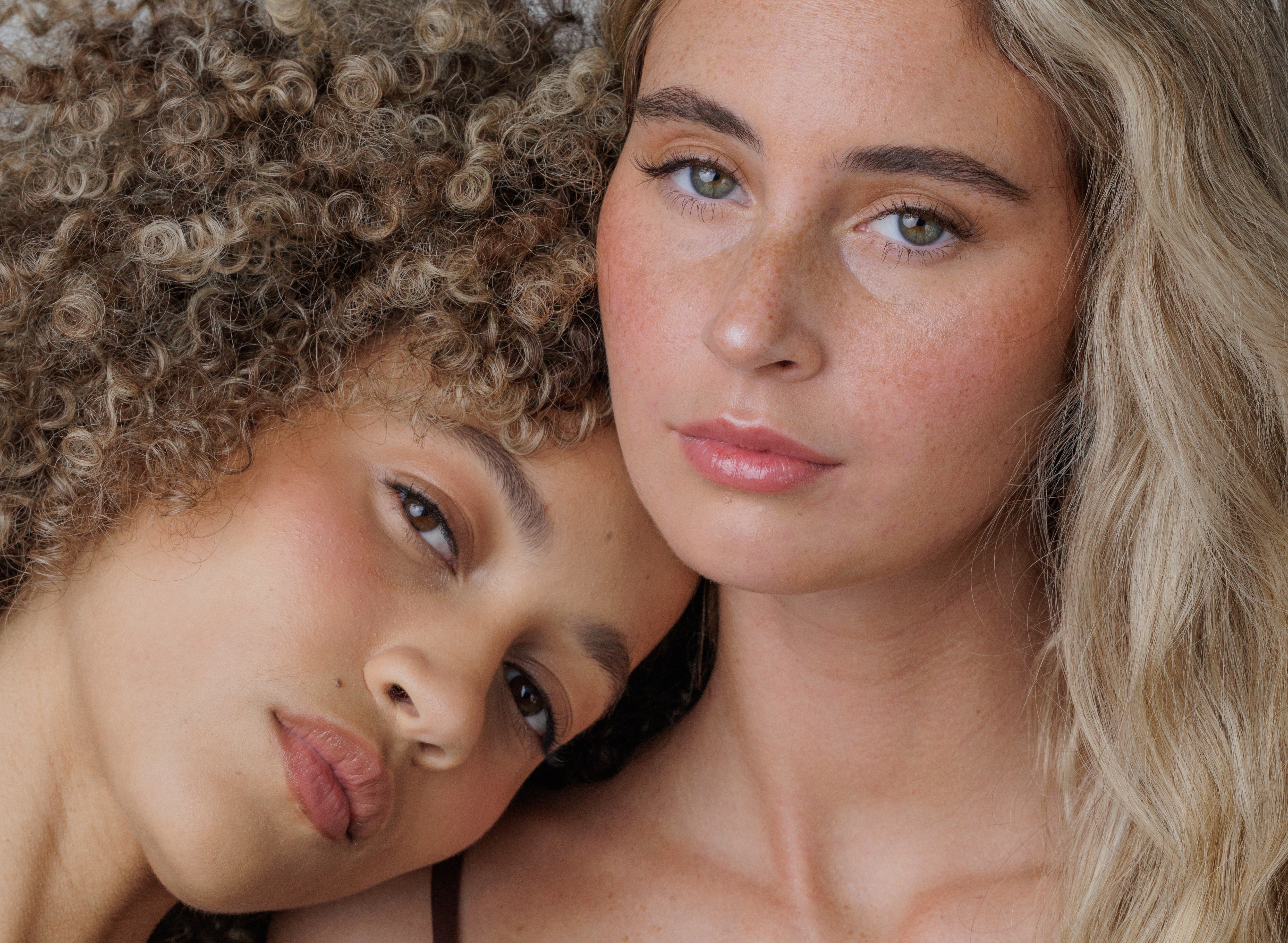 Two women with close-up of their faces, one with curly hair and the other with straight hair.