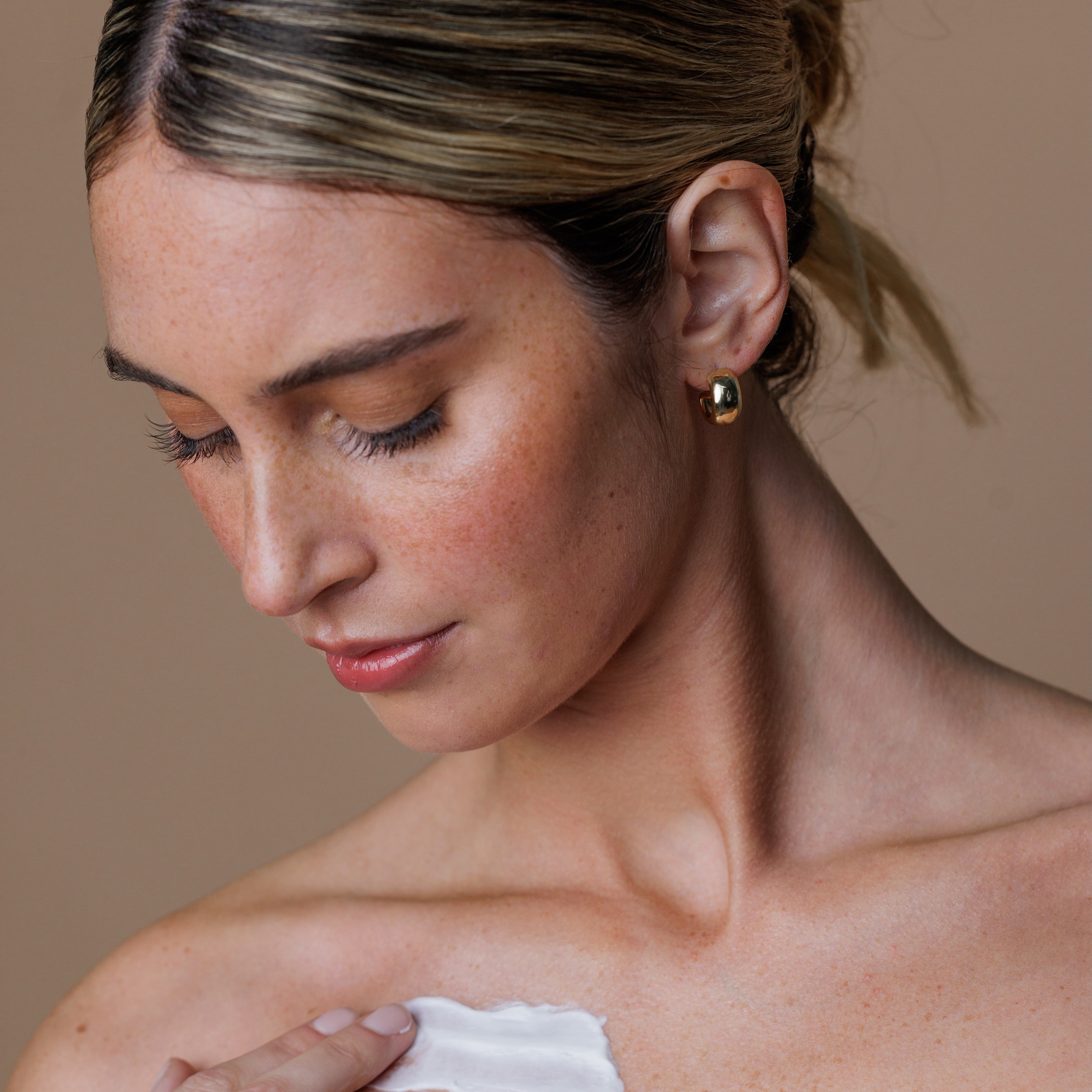 Woman applying sunscreen to her shoulder against a neutral background