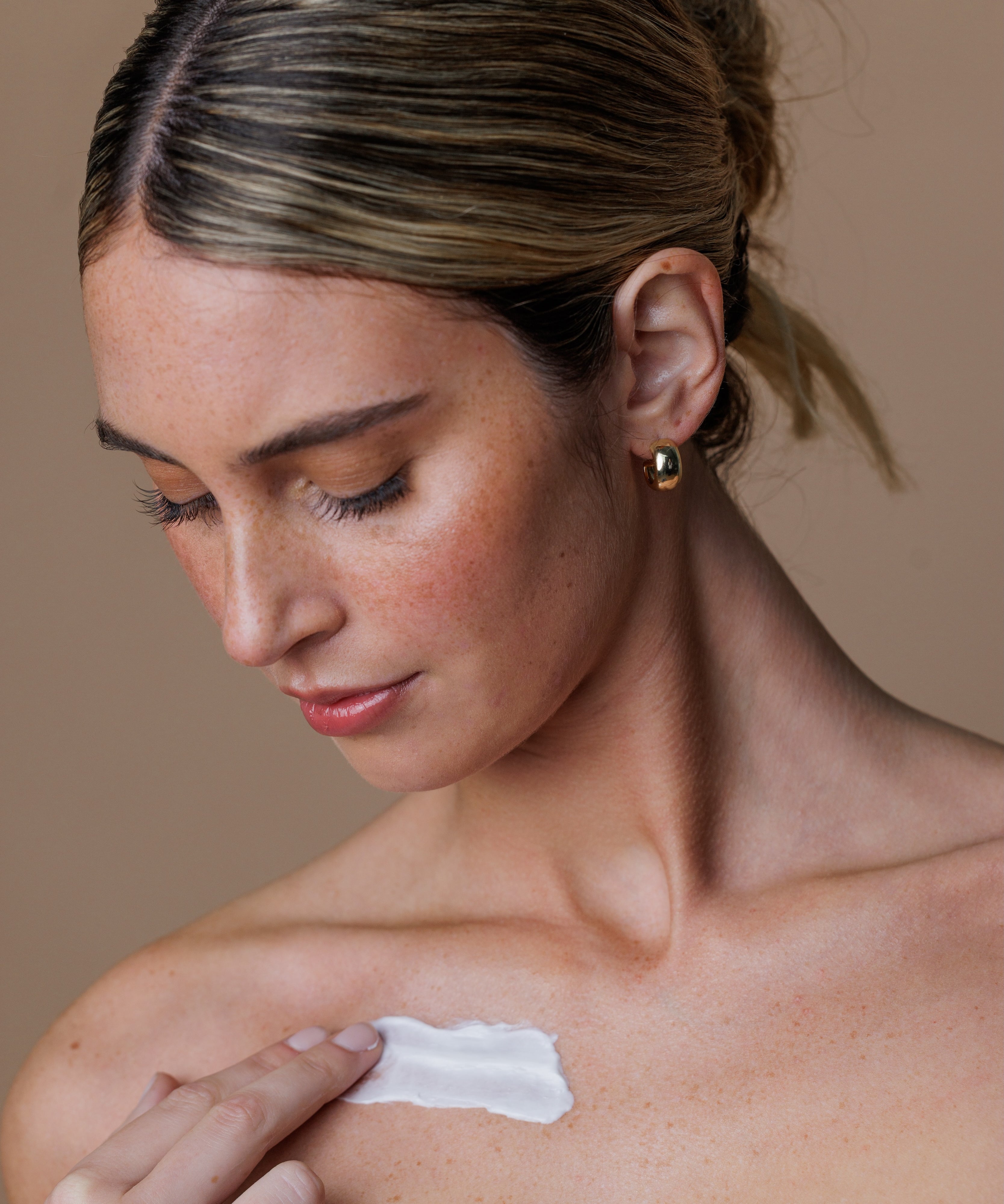 Woman applying sunscreen to her shoulder against a neutral background