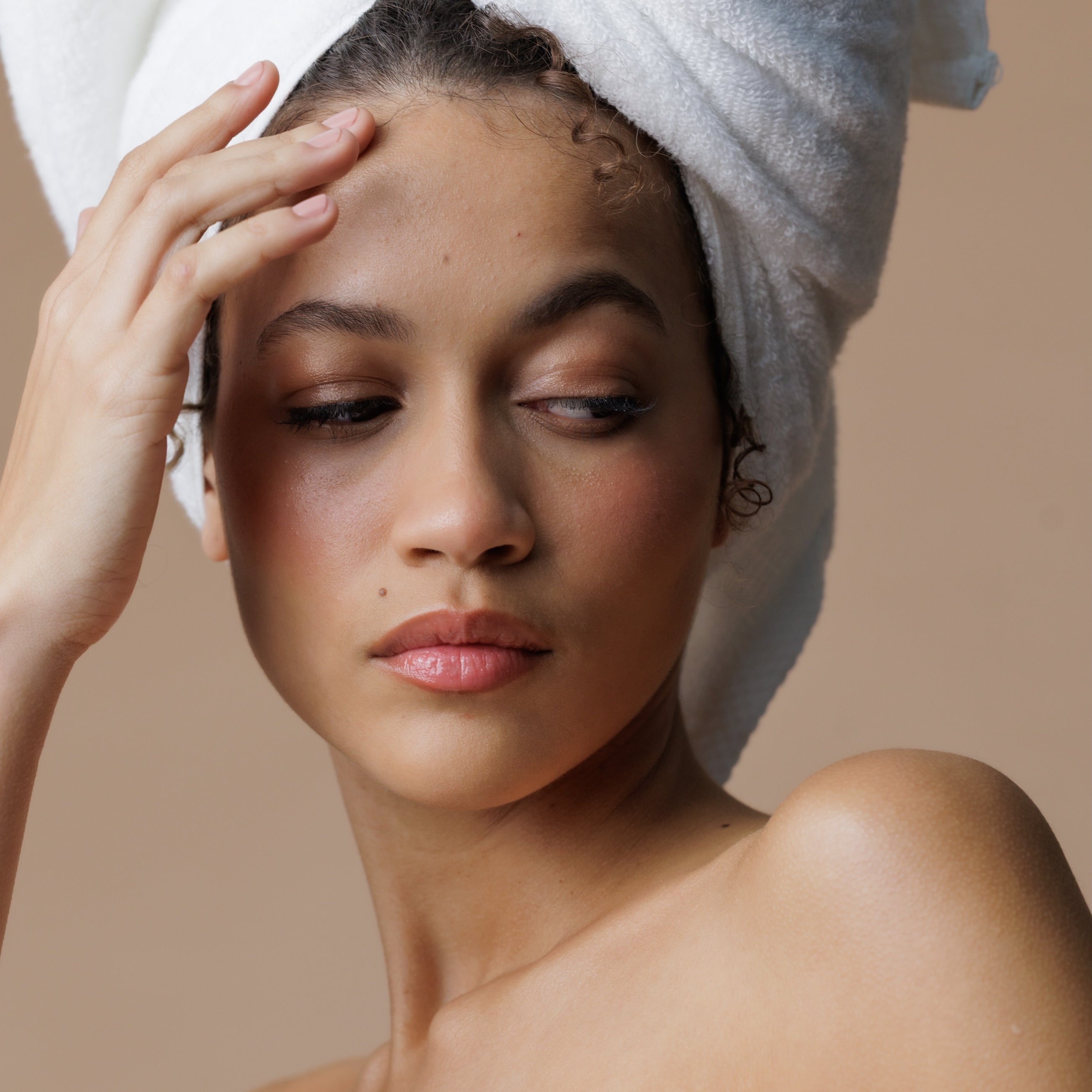 Woman with a towel wrapped around her head against a beige background