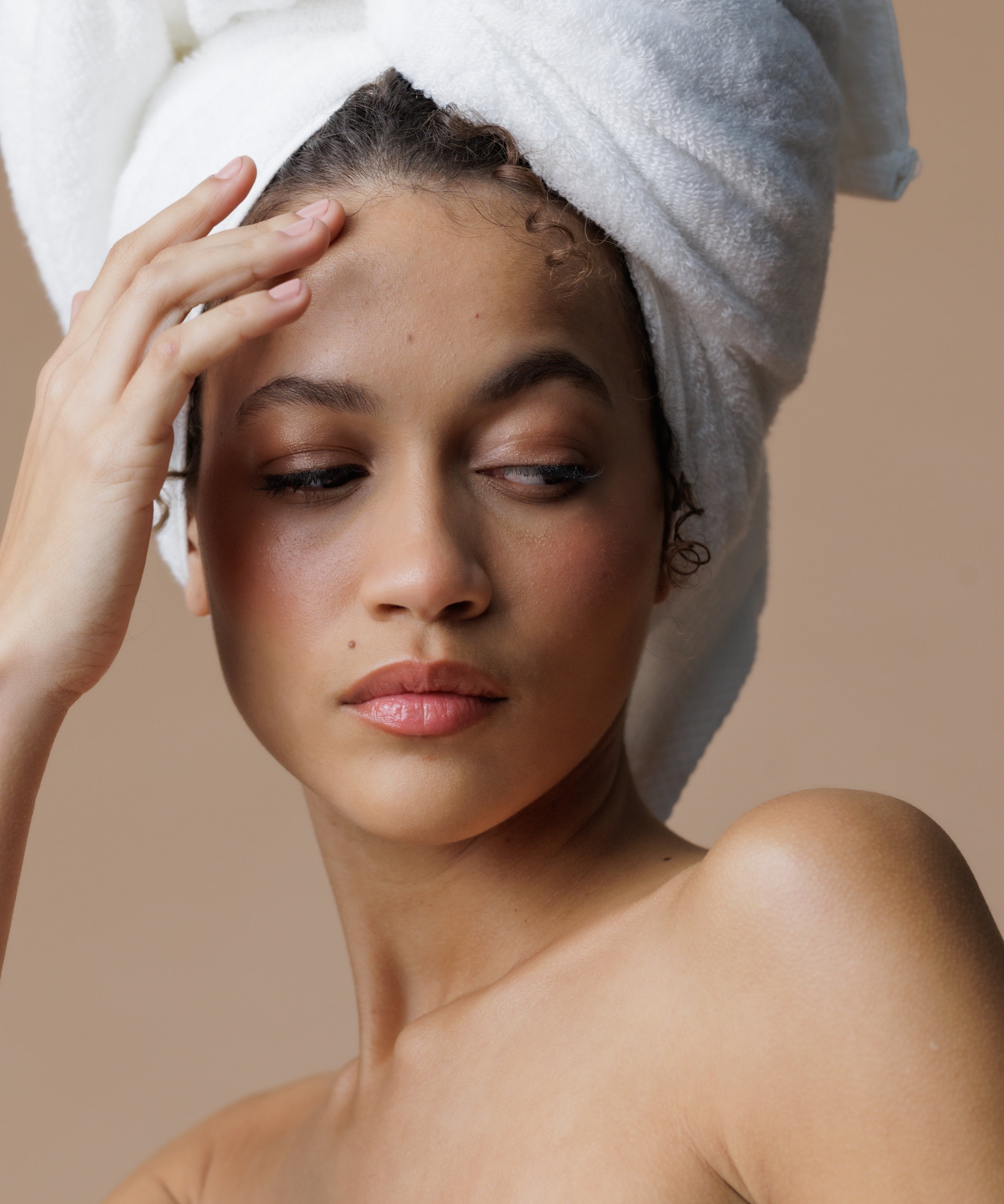 Woman with a towel wrapped around her head against a beige background