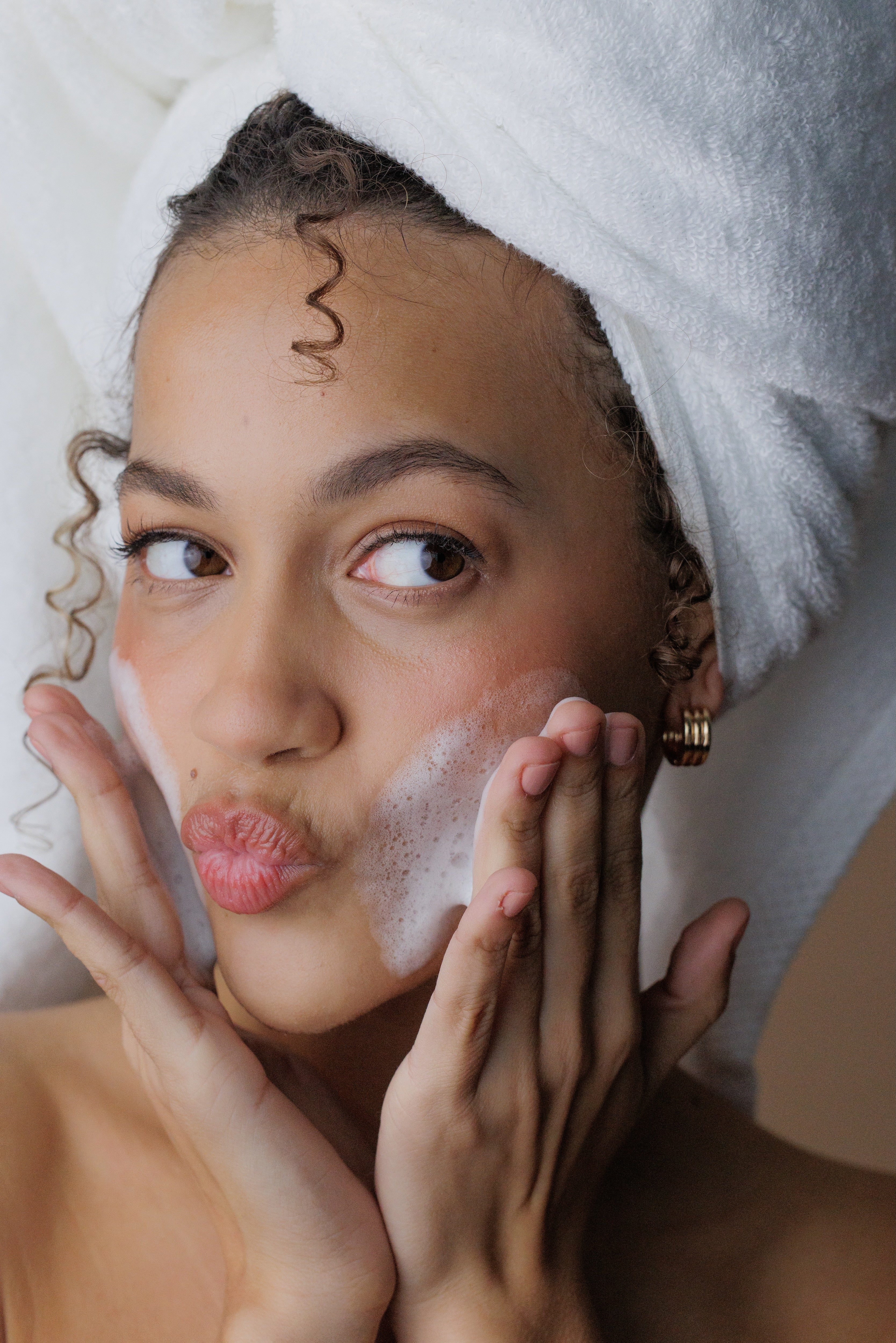 Woman with a towel on her head applying soap to her face