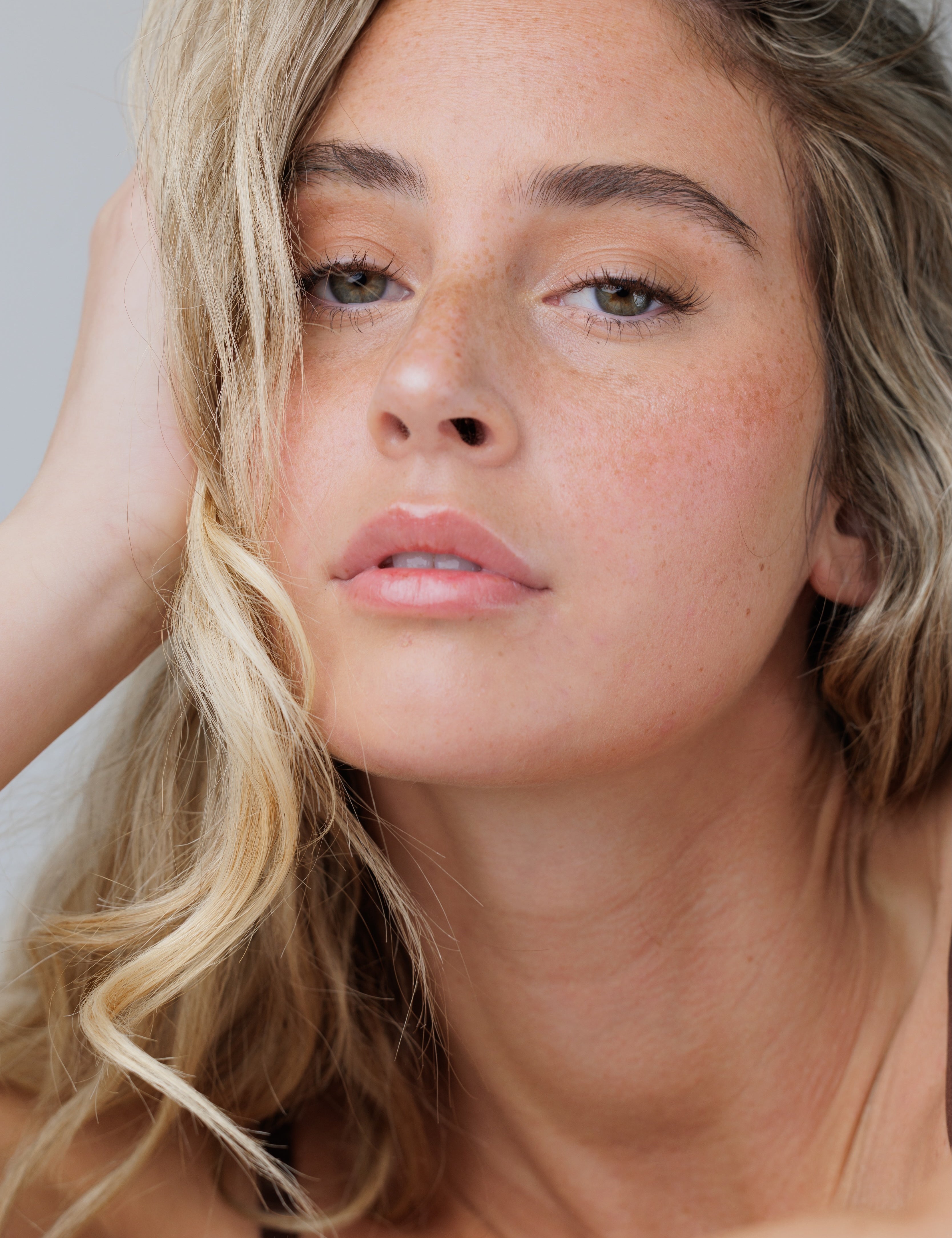 Close-up of a woman with blonde hair and freckles on a neutral background
