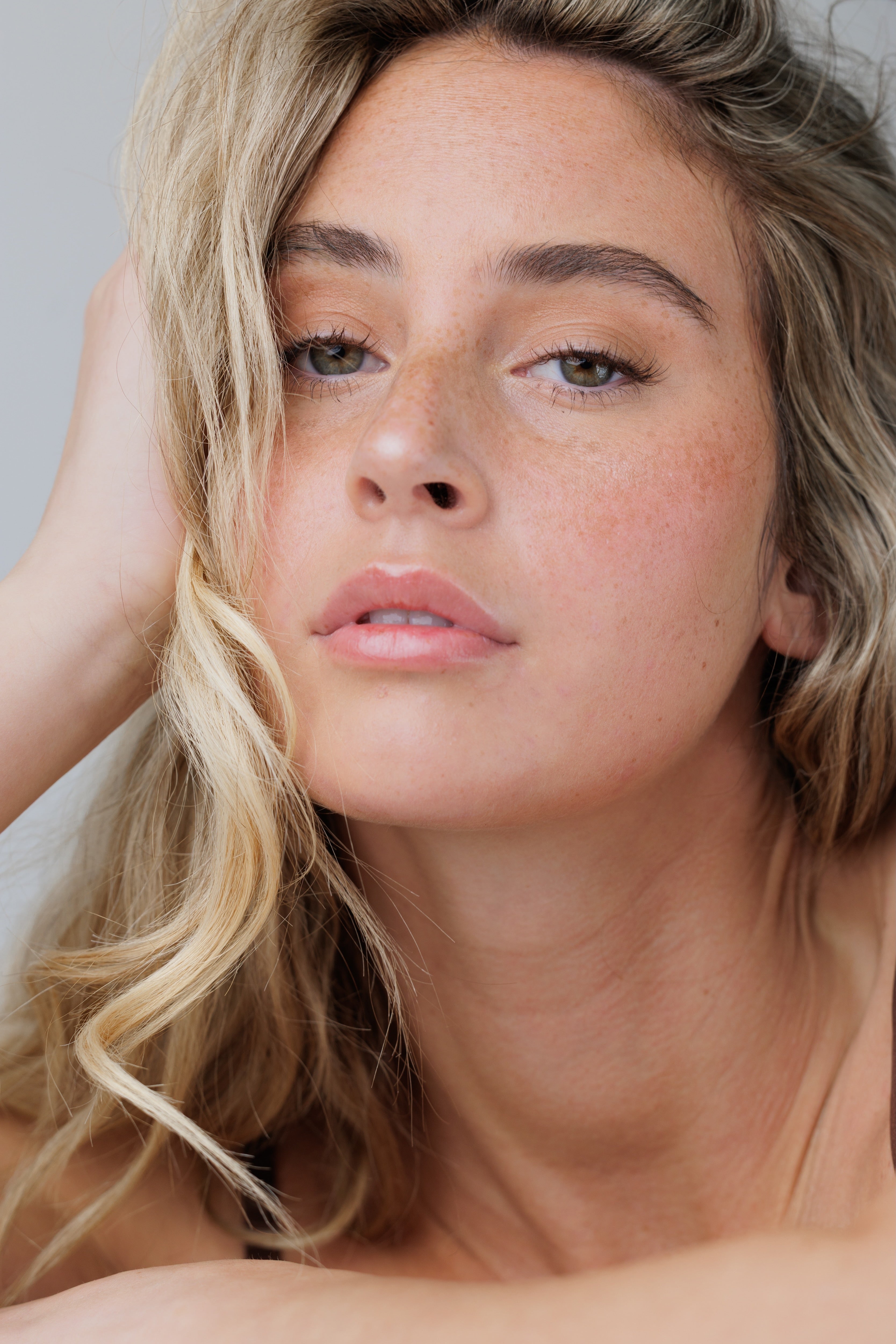 Close-up of a woman with blonde hair and freckles on a neutral background