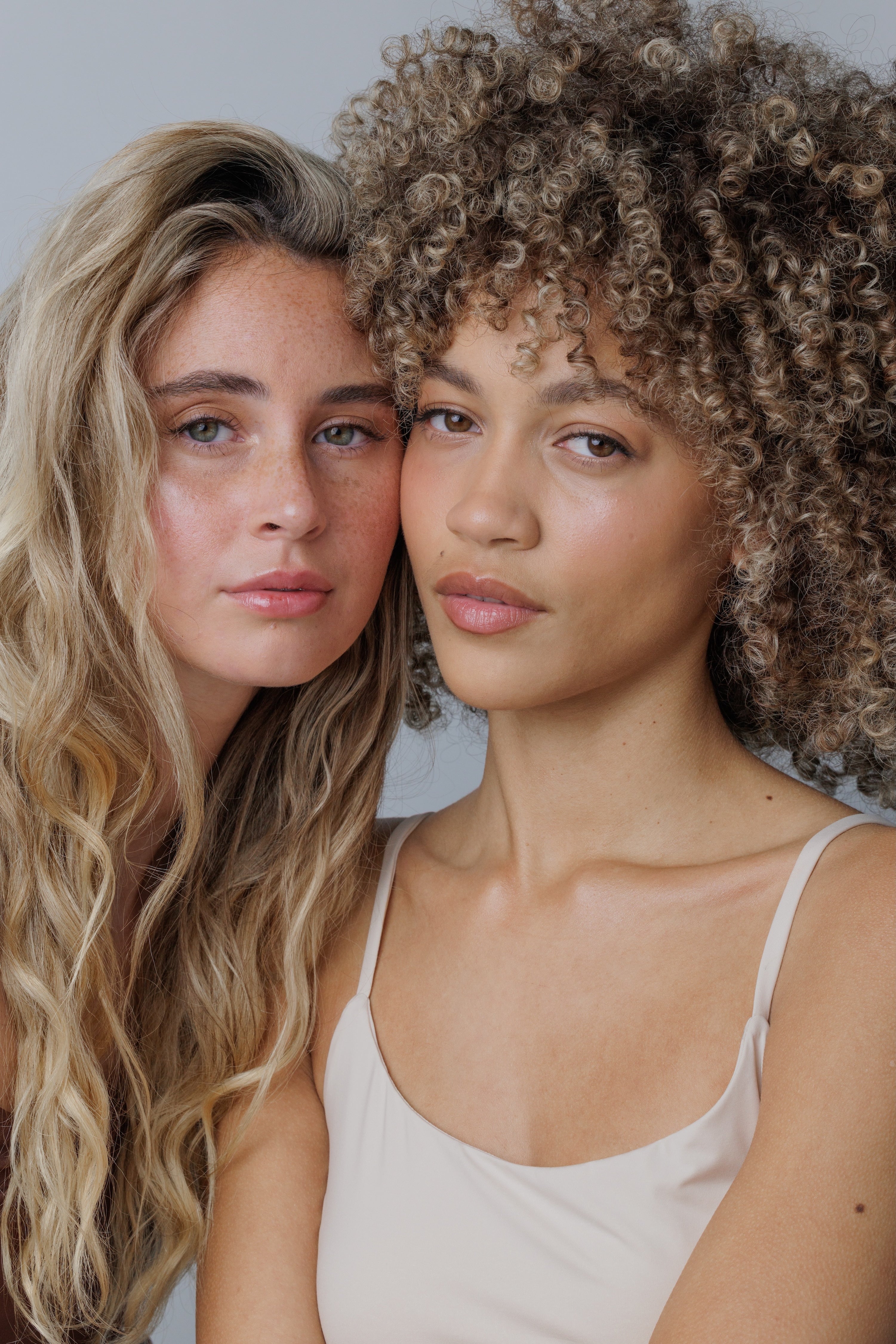Two women with curly hair standing close together against a neutral background