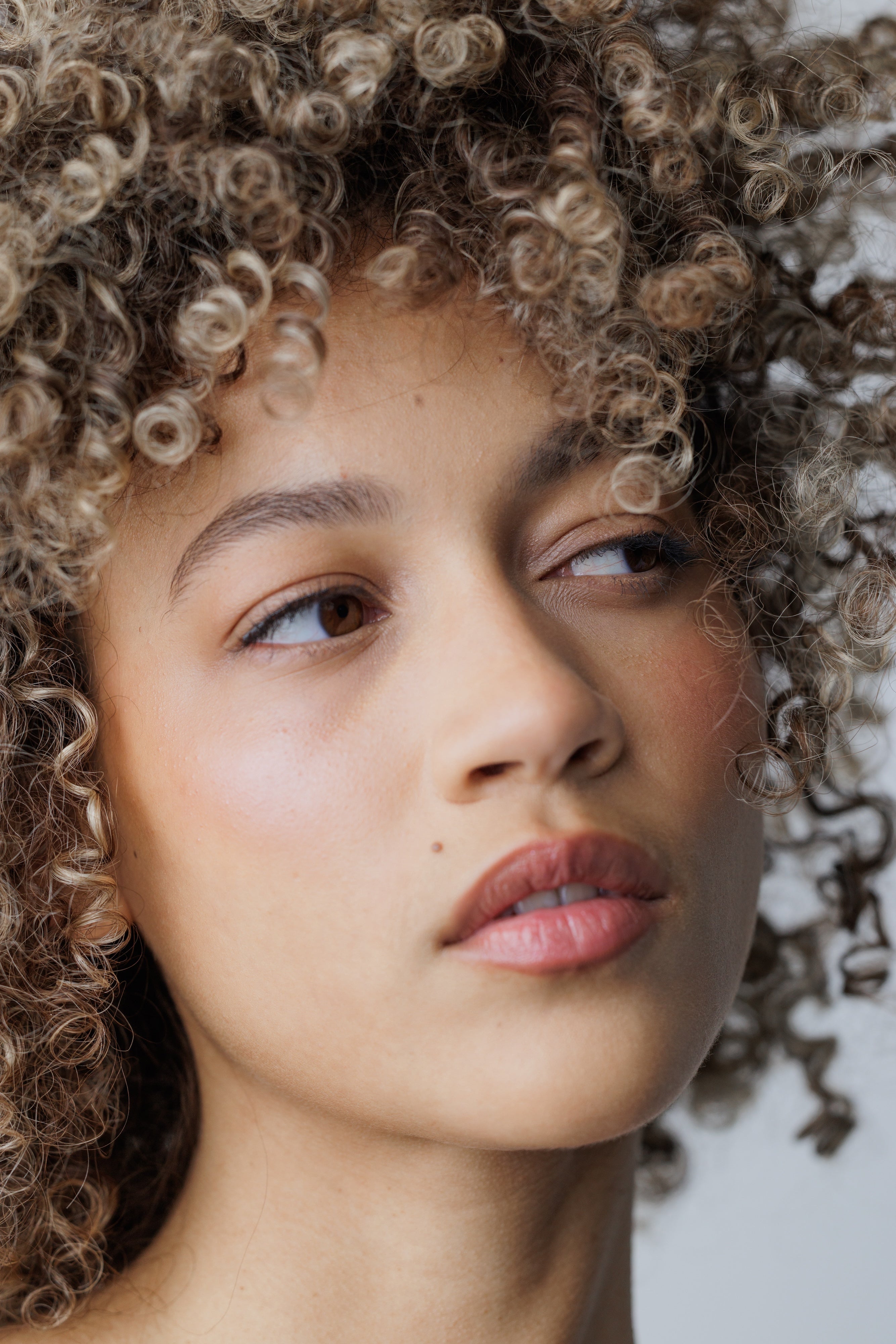 Close-up of a woman with curly hair against a neutral background