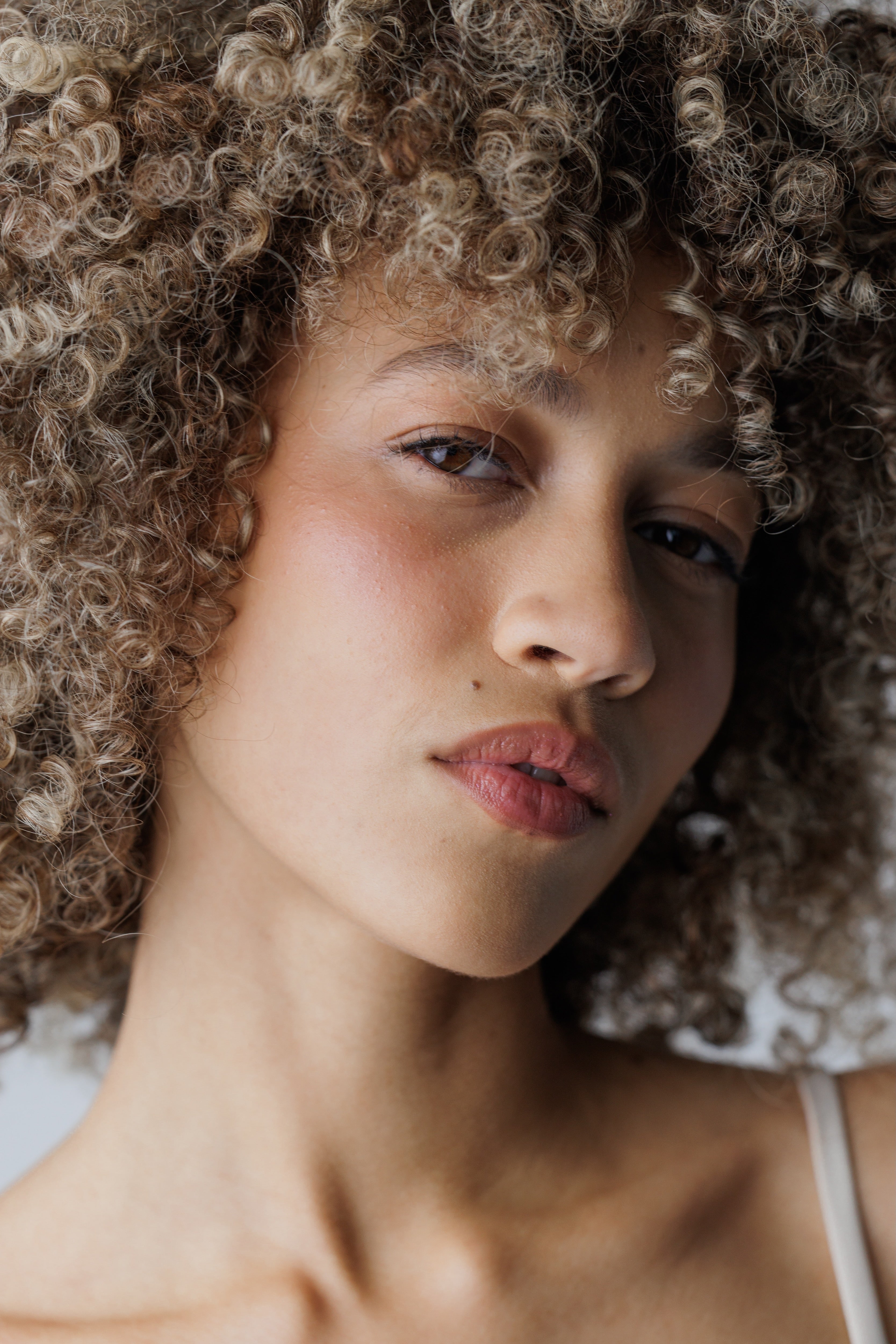 Close-up of a person with curly hair, wearing a white top.