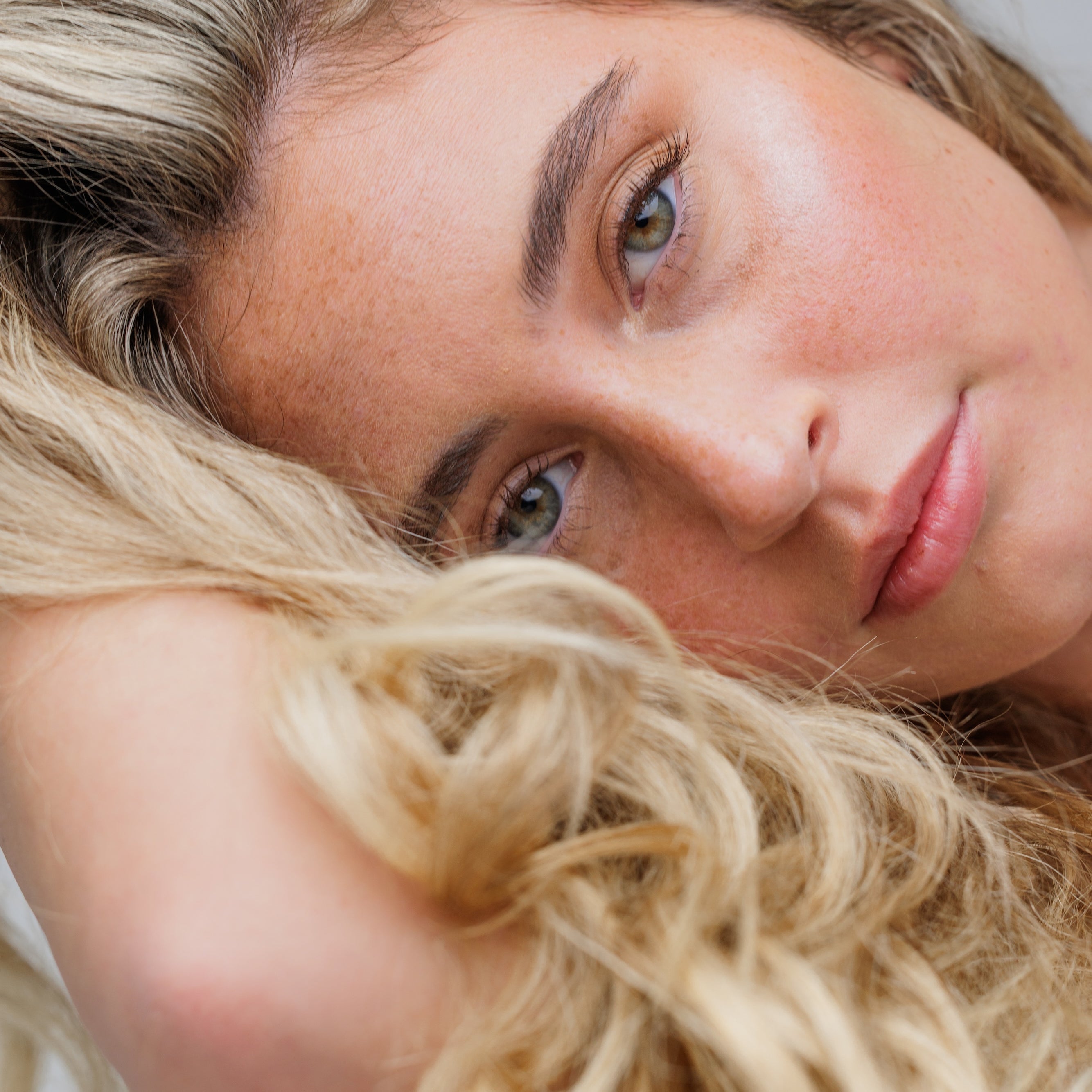 Close-up of a woman with blonde hair and blue eyes on a neutral background
